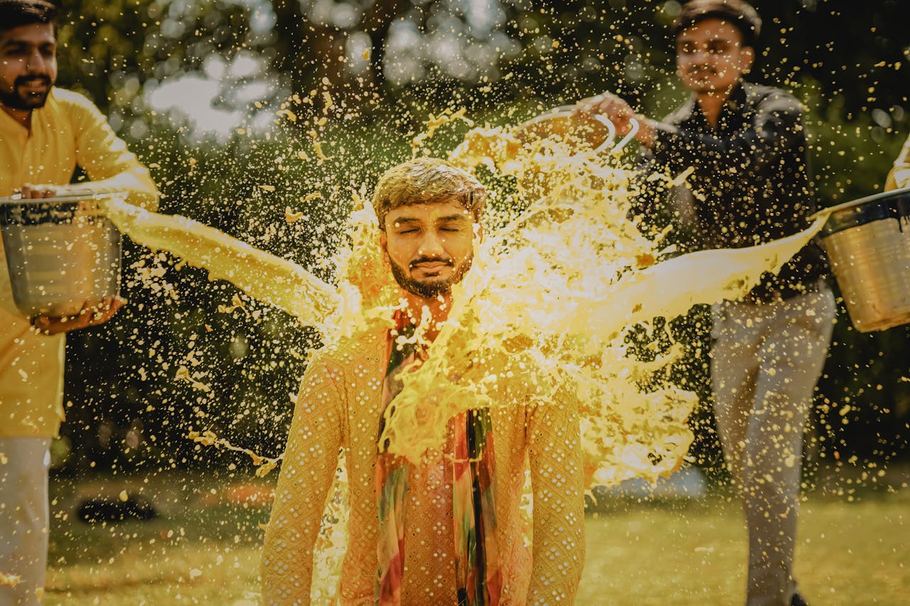Indian man involved in a traditional pre-wedding ritual with vibrant water splashing.